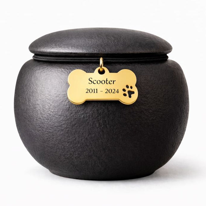 Zwarte, matte dierenurn met ronde vorm en subtiele structuur, afgewerkt met een goudkleurige pootafdruk en engelenvleugel