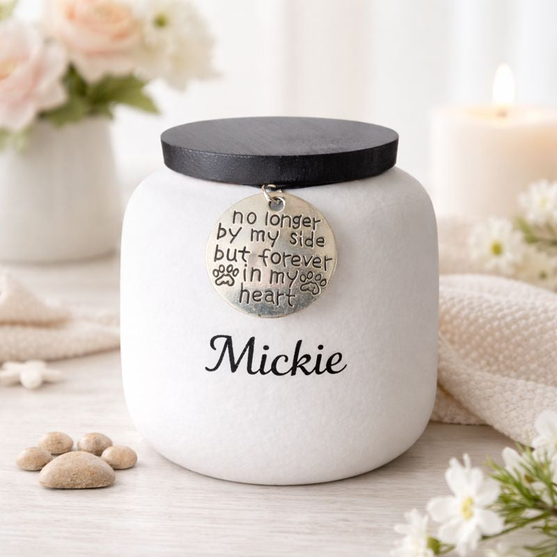 Witte keramische dierenurn met zwarte deksel en herdenkingshanger met pootafdruk.