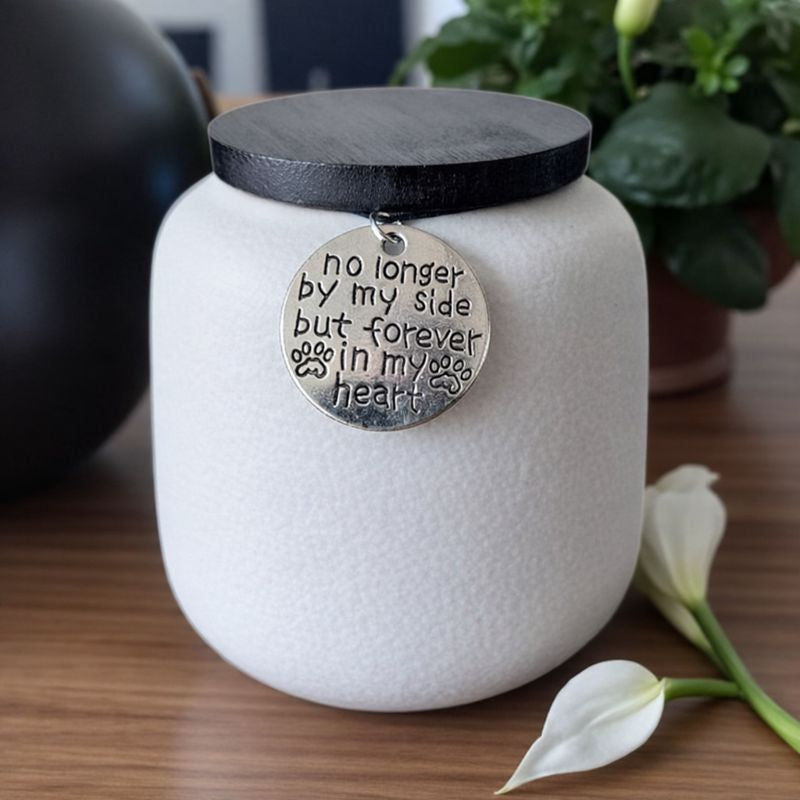 Witte keramische dierenurn met zwarte deksel en herdenkingshanger met pootafdruk.