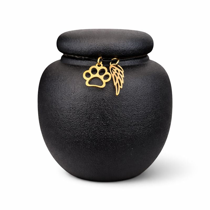 Zwarte keramische mini dierenurn met matte afwerking, ronde vorm en deksel, voorzien van gouden pootafdruk en engelenvleugel.