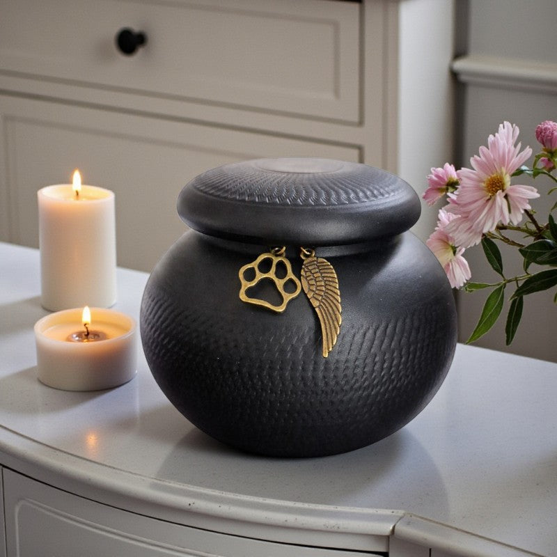 Matzwarte dierenurn met subtiele textuur en deksel met bronskleurige hangers