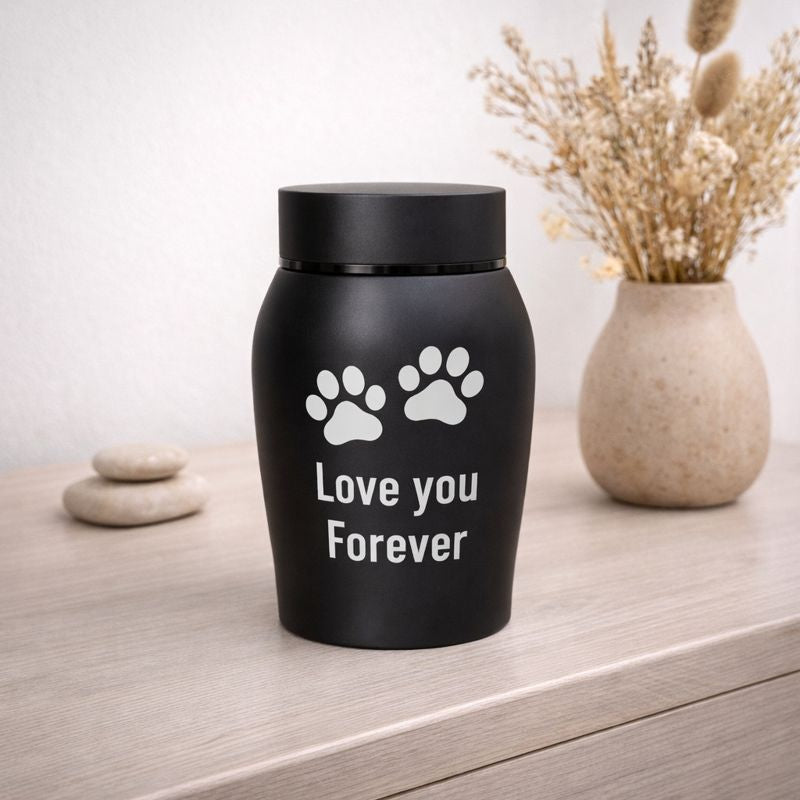 Zwarte dierenurn met pootafdrukken op houten dressoir met droogbloemen