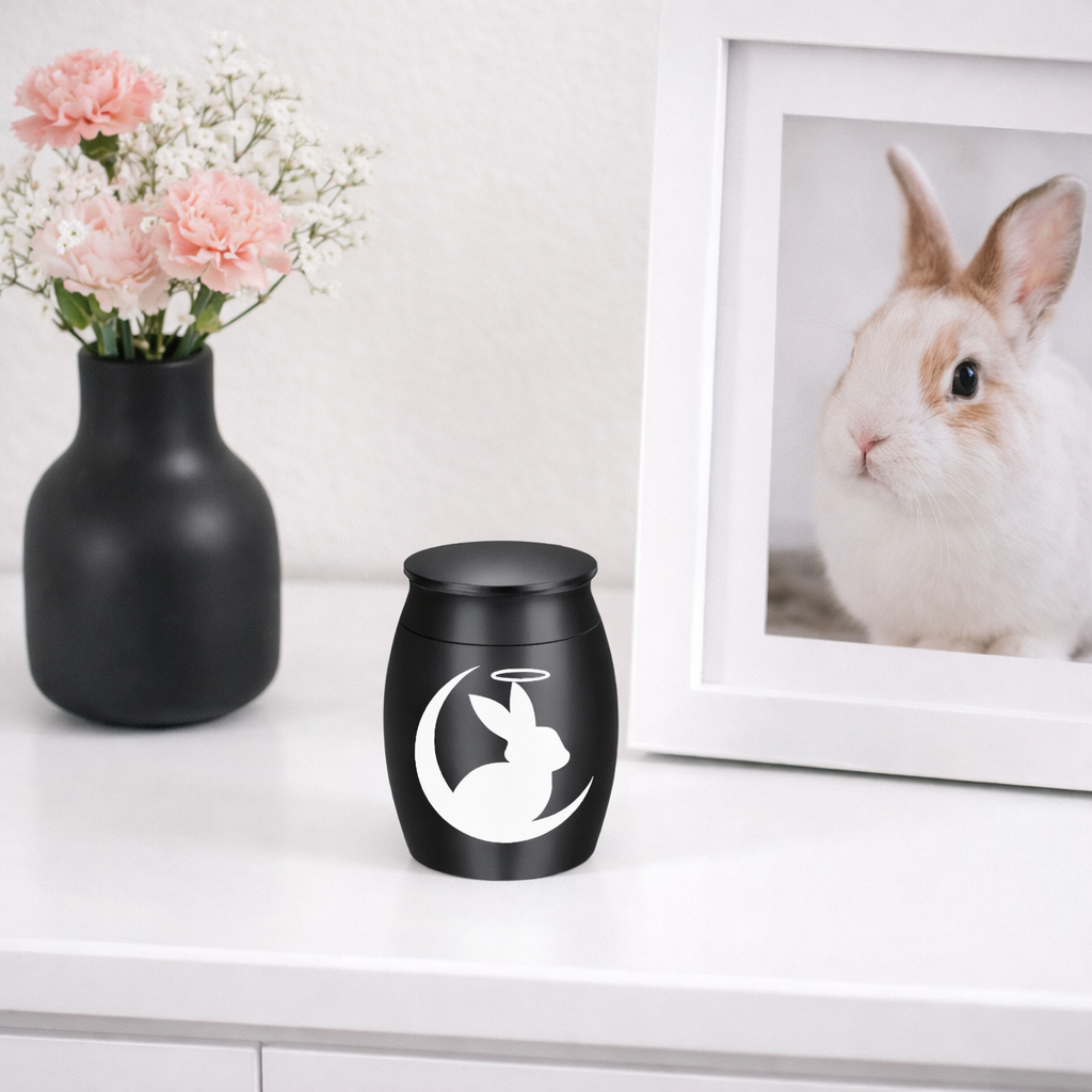 De laatste aai mini urn voor konijn van matzwart RVS met wit silhouet van een konijntje in de maan op een witte kast.