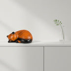 De laatste aai kattenurn in de vorm van een slapende kat met een realistische houtlook op een witte kast.