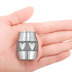 De laatste aai zilverkleurige RVS mini urn met hartjesmotief in een handpalm voor as of een plukje haar