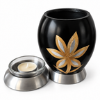 De laatste aai zwarte aluminium mini urn met goud-zilveren lelie motief en glazen waxinelichthouder voor asbewaring.