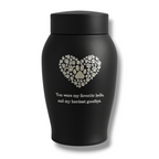 Zwarte matte urn met hart van pootafdrukken en troostende tekst, gefotografeerd tegen een lichte achtergrond.

